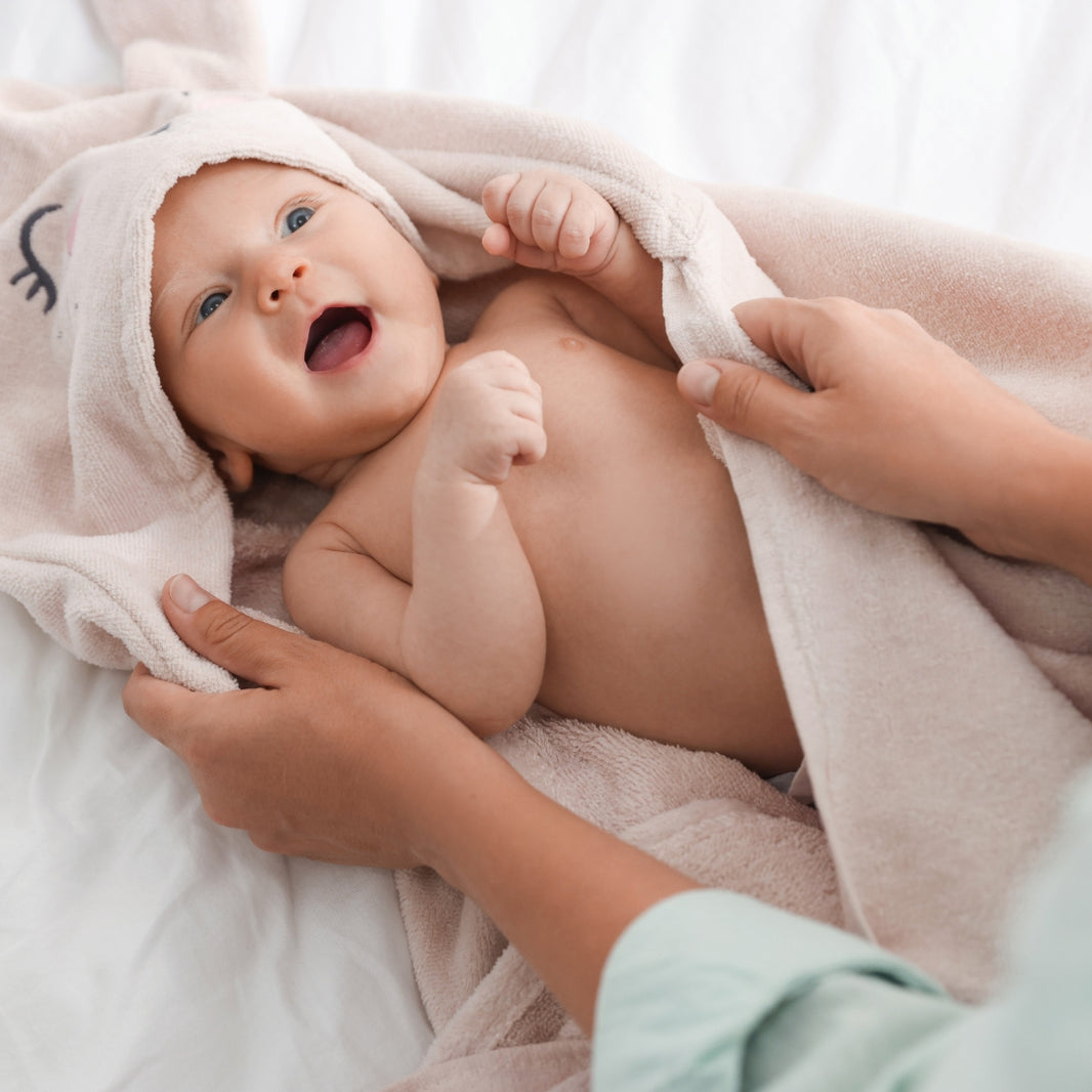 Baby wrapped in a towel with a person's hands holding it, on a soft white background